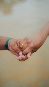 Close-up of two hands clasped together, one wearing a gold ring on the ring finger and a blue-green woven bracelet on the other wrist.