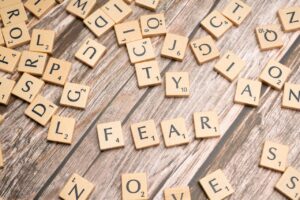 Scrabble tiles scattered on a wooden table, several letters visible including the word 'FEAR' formed by tiles on the surface